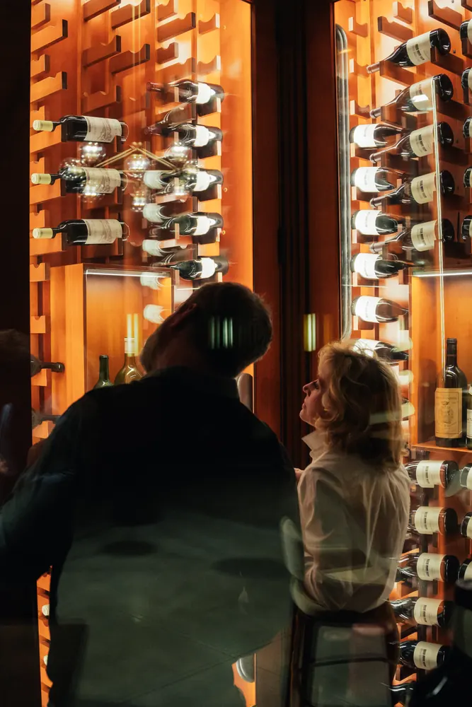 two people beside a lit wall of wine bottles